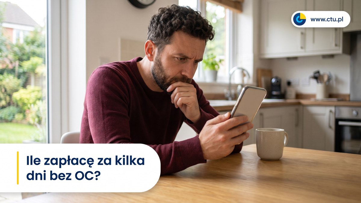 Mężczyzna siedzi przy kuchennym stole i z napięciem patrzy na ekran telefonu.